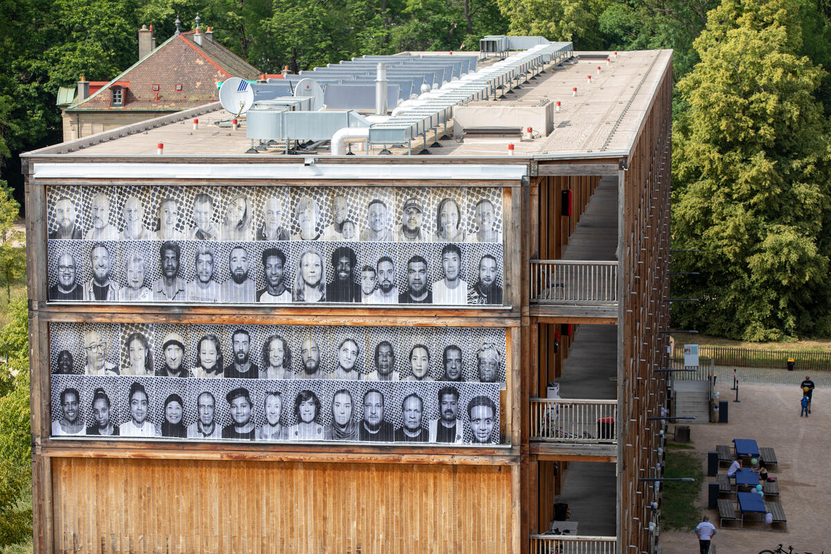 Rows of large scale portraits hang from the facade of a building in central Geneva.